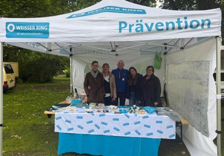Mitarbeiter*innen der Außenstelle Herne an einem Informationsstand mit Merchandise und Informationsflyern der Organisation WEISSER RING beim SPD-Familienfest Herne unter einem Zelt mit dem Logo des WEISSEN RINGS.